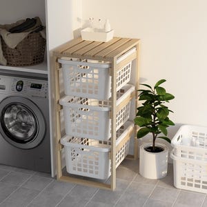 May include: A wooden laundry sorter with three white plastic baskets. The sorter has a slatted top and a natural wood finish. A washing machine and a plant in a white pot are nearby.