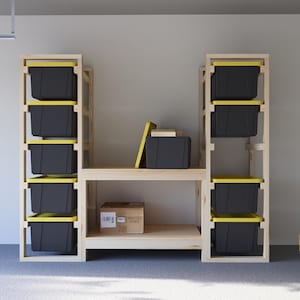 May include: A wooden storage shelf unit with multiple levels. The unit has two vertical sections with black storage bins with yellow lids. A central shelf holds additional storage items. The unit is made of light-colored wood.