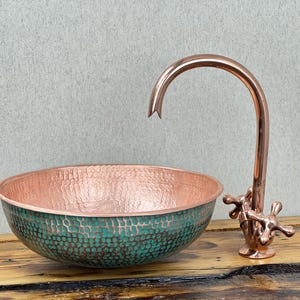 May include: A copper sink with a hammered finish and a green patina. The sink is paired with a copper faucet with cross-shaped handles.