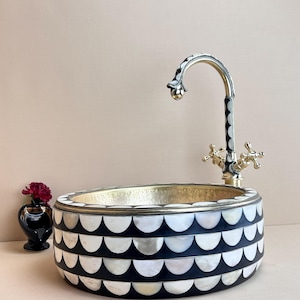 May include: A round, black and white sink with a brass faucet. The sink is made of mother of pearl and has a geometric pattern.
