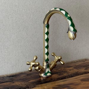 Può includere: Un rubinetto dorato con un design a motivi verdi e bianchi. Il rubinetto ha due maniglie e un becco alto.