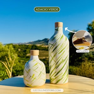 May include: Two white ceramic bottles with light green brushstroke patterns and light wood stoppers. The taller bottle is slender, while the shorter one is rounded. An inset shows oil pouring from a bottle onto bread with the text INCLUDED.