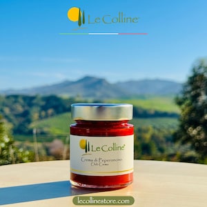 Könnte beinhalten: Ein Glas mit roter Chilicreme und einem silbernen Deckel. Das Glas hat ein weißes Etikett mit dem Text "Le Colline" und "Crema di Peperoncino Chili Creme".
