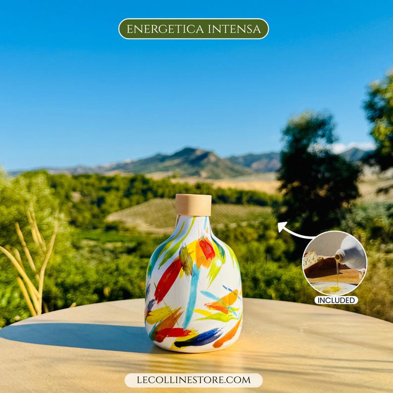 May include: A white ceramic bottle with a rounded base and a light brown stopper, featuring colourful abstract brushstrokes in red, yellow, blue, and green. The text ENERGETICA INTENSA appears at the top, and LECOLLINESTORE.COM is at the bottom.