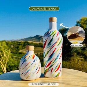 May include: Two white ceramic bottles with a colourful abstract brushstroke pattern in red, blue, green, and yellow. Both bottles feature a light wood-toned stopper. The text ADAGIO INTENSA and LECOLLINESTORE.COM are visible on the image.