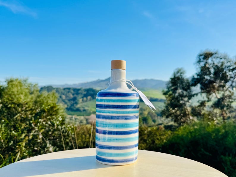 Handgefertigte Keramikflasche 500ml mit glatter weißer Oberfläche, verziert mit eleganten blauen Linien. Mittelgroß, perfekt für Öl oder Essig, verleiht Ihrer Küche einen mediterranen Touch. Die Textur ist glänzend und leicht zu handhaben.