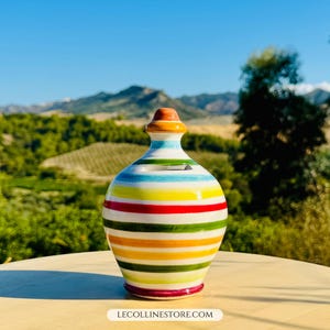 Könnte beinhalten: Eine Keramik-Spardose mit farbenfrohem Streifendesign. Die Spardose hat horizontale Streifen in verschiedenen Farben, darunter Gelb, Rot, Grün und Blau. Sie hat einen kleinen Schlitz oben und einen abgerundeten Deckel mit einem braunen und orangefarbenen Knauf.