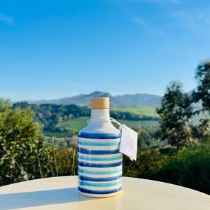 Handgefertigte Keramikflasche 250 ml mit glatter weißer Oberfläche, verziert mit eleganten blauen Linien. Klein, perfekt für Öl oder Essig, verleiht Ihrer Küche einen mediterranen Touch. Die Textur ist glänzend und leicht zu handhaben.
