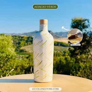 May include: A white ceramic bottle with a light green and yellow abstract brushstroke pattern and a light brown wooden stopper. The text ADAGIO VERDE is at the top, and LECOLLINESTORE.COM is at the bottom. An inset shows a pouring spout included.