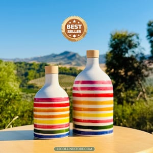 May include: Two white ceramic bottles with horizontal stripes in pink, red, orange, yellow, green, and blue. Each bottle features a light brown wooden stopper. The text BEST SELLER appears above the bottles, and LECOLLINSTORE.COM is below.