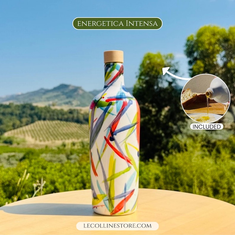 May include: A white bottle with a colourful abstract brushstroke pattern in red, blue, green, and yellow, topped with a light brown wooden stopper. The text ENERGETICA INTENSA appears above, and LECOLLINESTORE.COM is printed at the bottom.