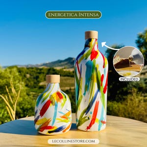 Due bottiglie in ceramica bianca con pennellate colorate di rosso, blu, giallo e verde. Le bottiglie hanno tappi in legno e il testo "ENERGETICA INTENSA" è in alto.
