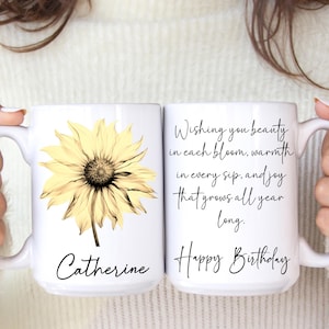 May include: Two white ceramic mugs. One mug features a yellow sunflower graphic and the name "Catherine". The other mug has the text "Wishing you beauty in each bloom, warmth in every sip, and joy that grows all year long. Happy Birthday."
