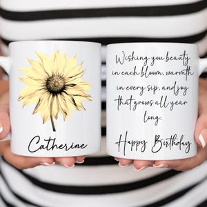 May include: White ceramic mug featuring a yellow sunflower design and the name "Catherine" in black script. The other side of the mug has the text "Wishing you beauty in each bloom, warmth in every sip, and joy that grows all year long. Happy Birthday."