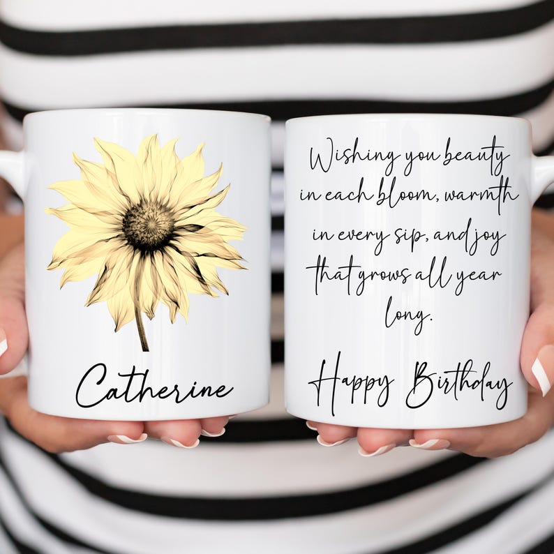 May include: White ceramic mug featuring a yellow sunflower design and the name "Catherine" in black script. The other side of the mug has the text "Wishing you beauty in each bloom, warmth in every sip, and joy that grows all year long. Happy Birthday."