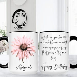 May include: White ceramic mug with a black handle and rim, featuring a pink flower design and the name "Abigail." The other side has the text "Wishing you beauty...Happy Birthday."