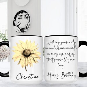 May include: White ceramic mug with a black handle and rim, featuring a yellow sunflower illustration and the name "Christine". The other side has the text "Wishing you beauty...Happy Birthday".