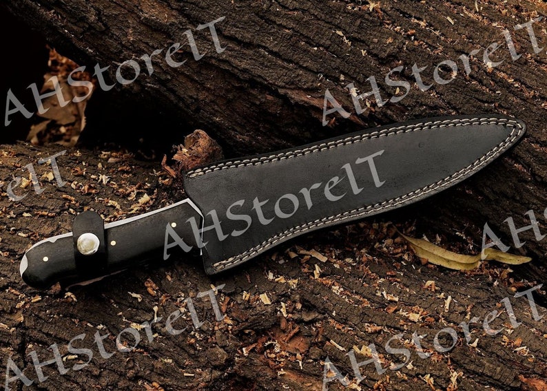 May include: A black leather sheath with a stitched edge and a silver blade knife with a black handle. The knife is on a wooden surface.