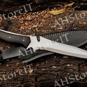 May include: A black-handled knife with a silver blade and a leather sheath. The knife has a unique design with a serrated edge and a pointed tip.