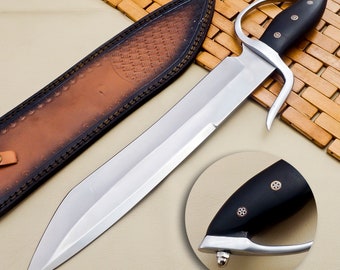 May include: A silver-colored sword with a black handle and a leather sheath. The handle has a decorative design with gold accents.