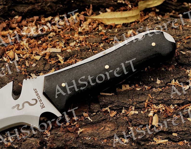 May include: A black handled knife with a silver blade. The blade has a serrated edge and a small hole near the handle. The handle is made of wood and has a brass pin. The knife has the word "Krauser" engraved on the blade.