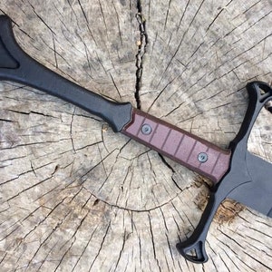 May include: A black and brown sword with a unique handle design. The sword is lying on a wooden surface.