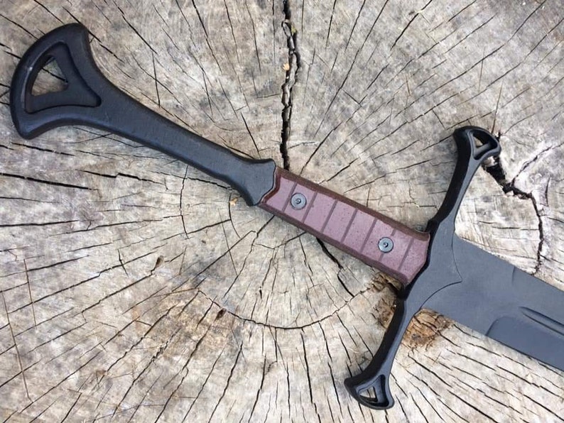 May include: A black and brown sword with a unique handle design. The sword is lying on a wooden surface.