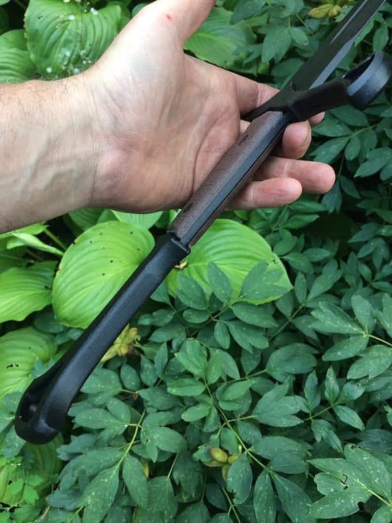 May include: A black and brown sword with a wooden handle. The sword is held in a hand, with the blade pointing towards the camera.