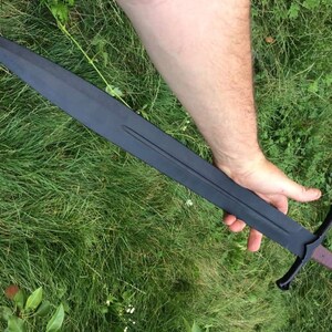 May include: A black sword with a wooden handle and a cross guard. The sword is held in a person's hand.
