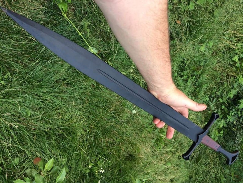 May include: A black sword with a wooden handle and a cross guard. The sword is held in a person's hand.