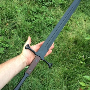 May include: A black sword with a brown wooden handle and a black metal guard. The sword is held in a person's hand.