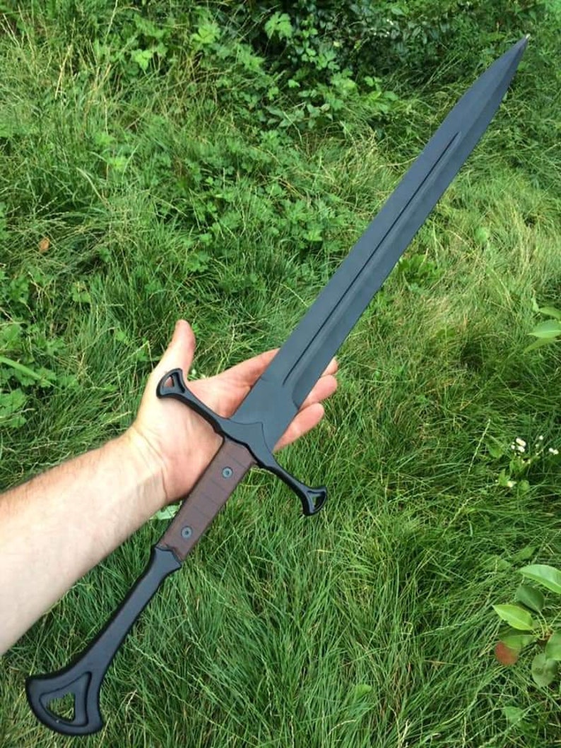 May include: A black sword with a brown wooden handle and a black metal guard. The sword is held in a person's hand.