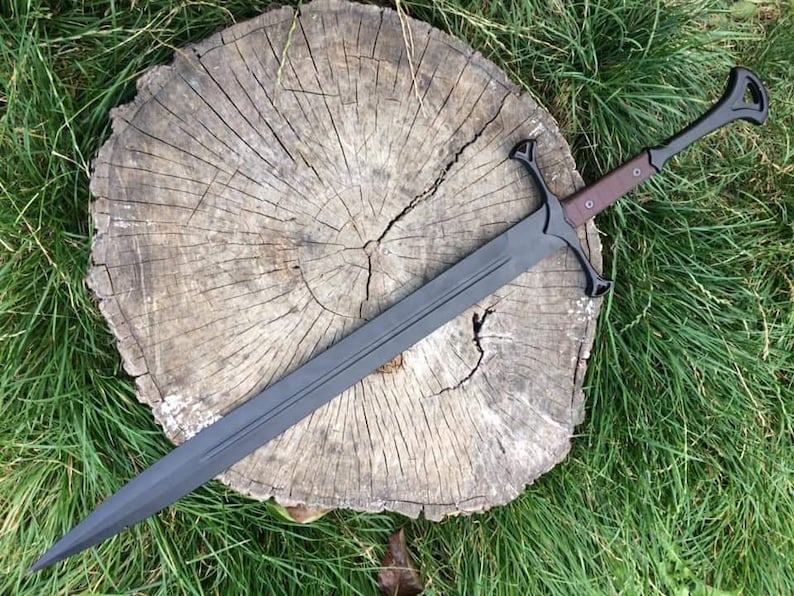 May include: A black sword with a brown handle and a black scabbard. The sword is resting on a wooden stump.