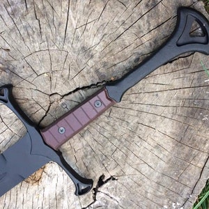 May include: A black sword with a brown handle and a decorative guard. The sword is lying on a wooden surface.