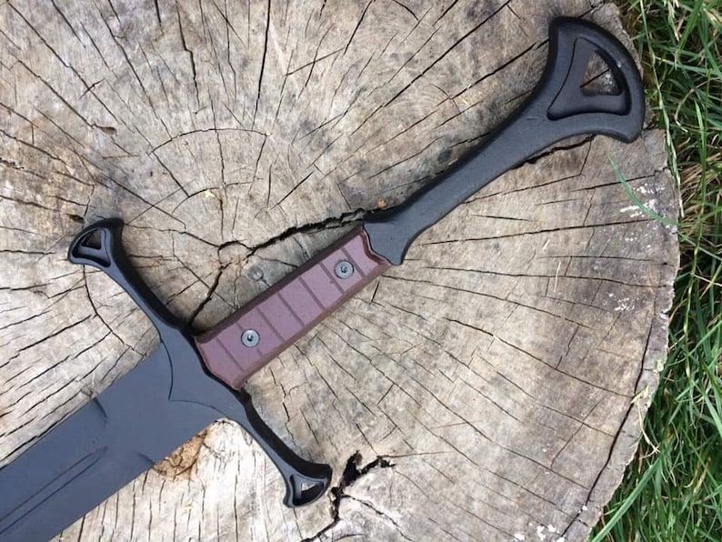May include: A black sword with a brown handle and a decorative guard. The sword is lying on a wooden surface.