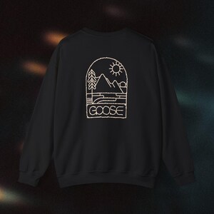 Puede incluir: Sudadera negra con un contorno blanco de una escena de montaña y la palabra "GOOSE" en una pancarta.