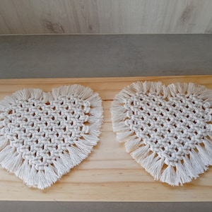 Peut inclure: Deux dessous-de-verre en crochet en forme de cœur blancs avec des franges. Les dessous-de-verre sont faits de cordon de coton et ont un design délicat et complexe.