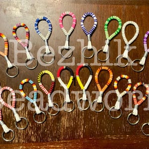 May include: A selection of beaded keyrings in a range of colours, including red, orange, yellow, blue, pink, and green. Each keyring has a loop design with a silver-coloured key ring. The word "Bezhki Headwork" is partially visible.