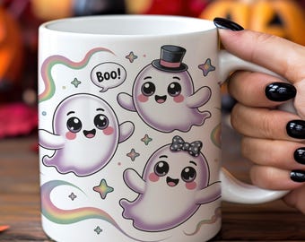 Puede incluir: Taza de cerámica blanca con tres fantasmas de dibujos animados con caras sonrientes y un diseño de arcoíris. Un fantasma lleva un sombrero de copa, otro un lazo, y uno dice "¡Boo!". La taza es sostenida por una persona con esmalte de uñas negro.
