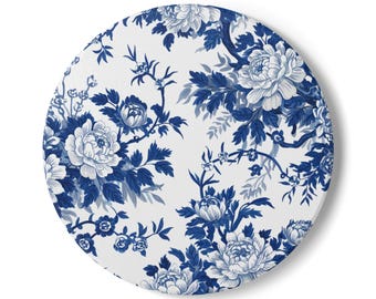 May include: Round white coaster with a blue floral pattern. The design features detailed blue flowers and foliage against a white background. The coaster is circular and has a smooth surface.