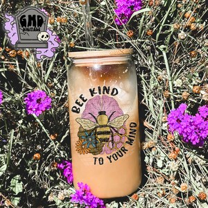 May include: A glass tumbler with a bamboo lid and a straw. The tumbler has a graphic of a bee, a honeycomb, and a brain with the text "Bee Kind To Your Mind".