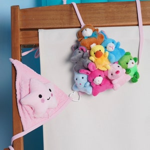 May include: A wooden crib with a white fabric panel and a collection of plush animal toys. The toys include a brown bear, blue bunny, yellow duck, and pink pig. A pink star-shaped decoration hangs on the side.