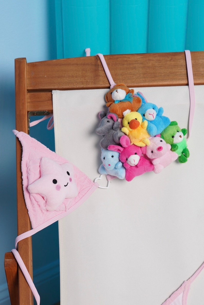 May include: A wooden crib with a white fabric panel and a collection of plush animal toys. The toys include a brown bear, blue bunny, yellow duck, and pink pig. A pink star-shaped decoration hangs on the side.
