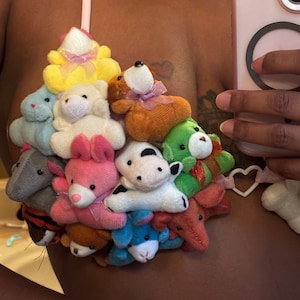 May include: A unique bra made of various small plush toys in assorted colors, including yellow, white, pink, and blue. The bra is held together with pink straps.