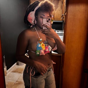 May include: A unique halter top made of small plush toys in various colors, including pink, yellow, blue, and green. The top is tied with pink string and paired with light-wash denim jeans.
