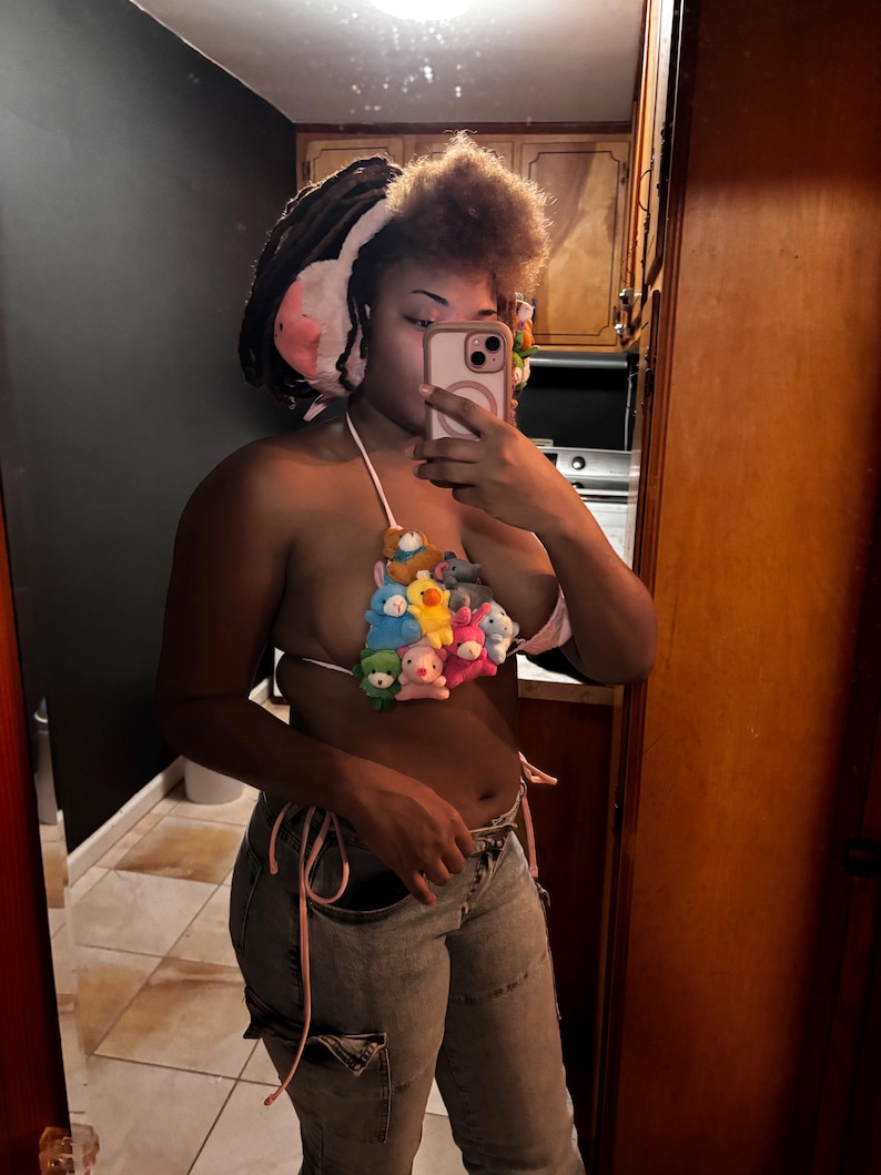 May include: A unique halter top made of small plush toys in various colors, including pink, yellow, blue, and green. The top is tied with pink string and paired with light-wash denim jeans.