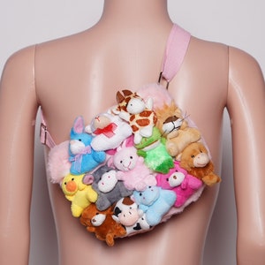 Pu&ograve; includere: Una borsa di peluche rosa ornata da numerosi peluche. La borsa ha un cinturino rosa ed &egrave; piena di varie creature di peluche, tra cui una giraffa, un leone, un orso e un coniglio. La borsa &egrave; progettata per essere indossata a tracolla.