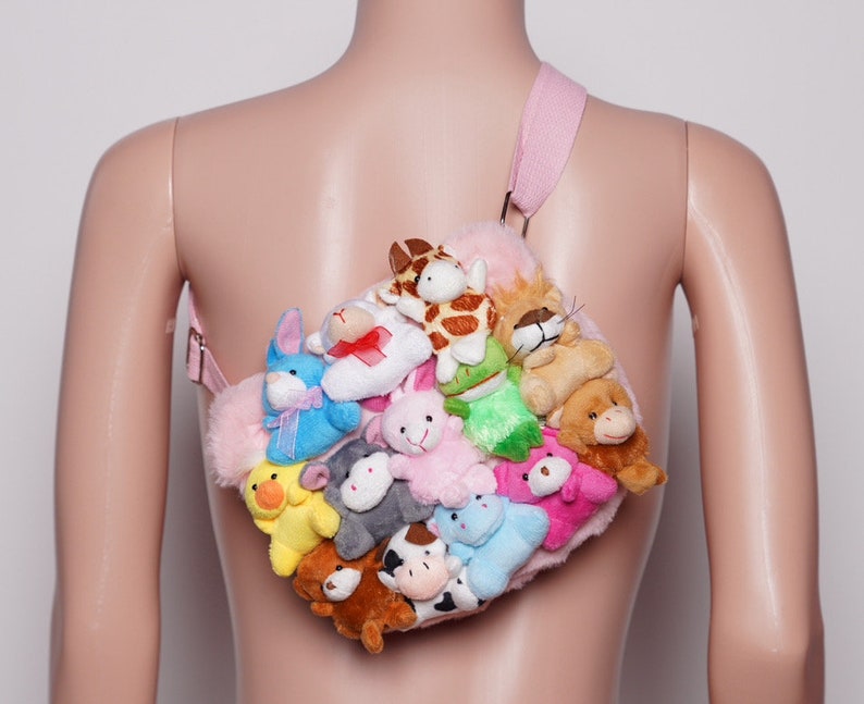 Pu&ograve; includere: Una borsa di peluche rosa ornata da numerosi peluche. La borsa ha un cinturino rosa ed &egrave; piena di varie creature di peluche, tra cui una giraffa, un leone, un orso e un coniglio. La borsa &egrave; progettata per essere indossata a tracolla.