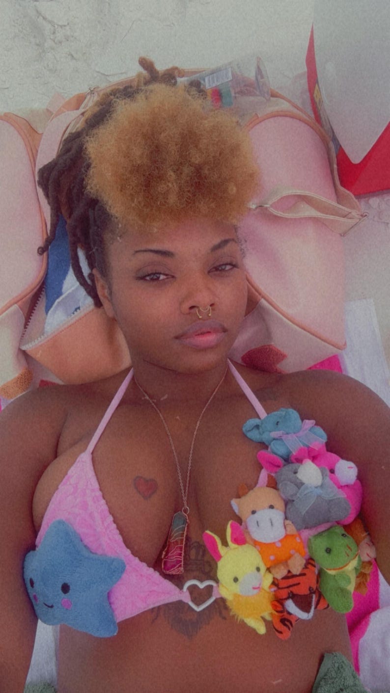 May include: Pink bikini top adorned with plush toy embellishments. The top features a heart-shaped pendant and a small heart tattoo. The plush toys include a blue star, a yellow bunny, and other colorful creatures.