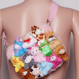 Pu&ograve; includere: Una borsa a tracolla in peluche rosa ornata da numerosi piccoli peluche. La borsa presenta una tracolla rosa chiaro e una variet&agrave; di peluche colorati, tra cui coniglietti, mucche e giraffe. La borsa &egrave; progettata per essere indossata a tracolla.